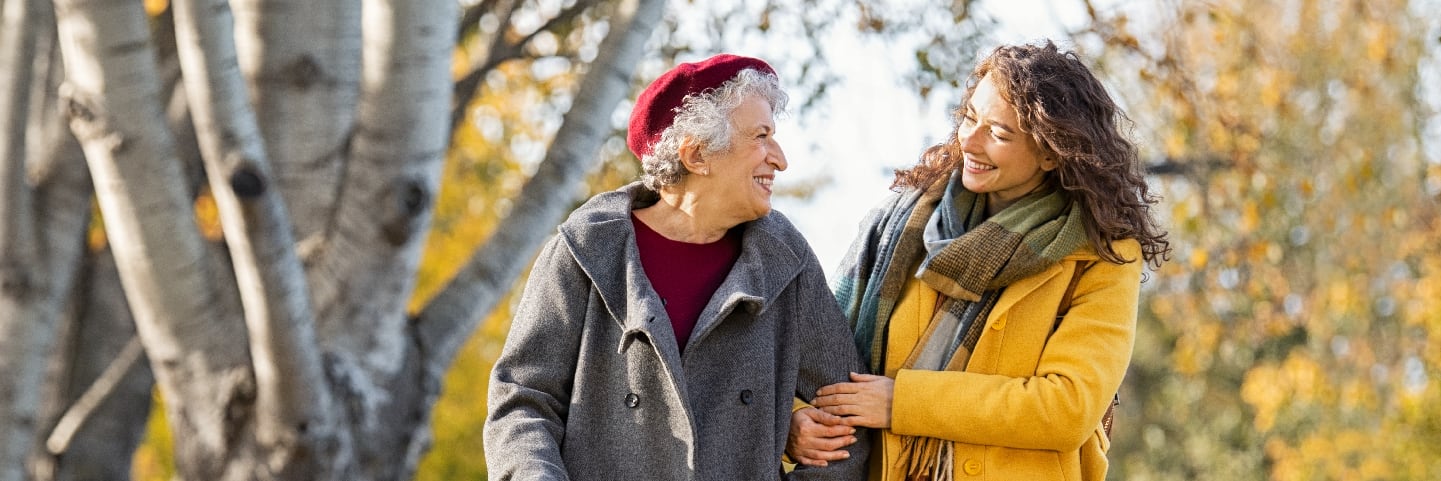 A senior and caregiver smiling outside.