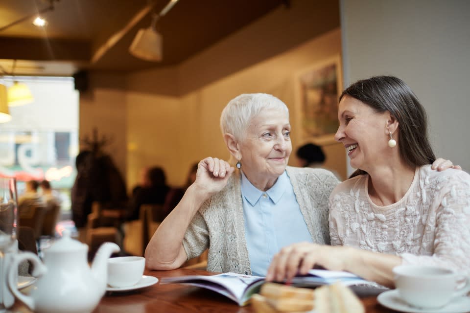 Senior woman sits with friend while looking over a book in a cafe.