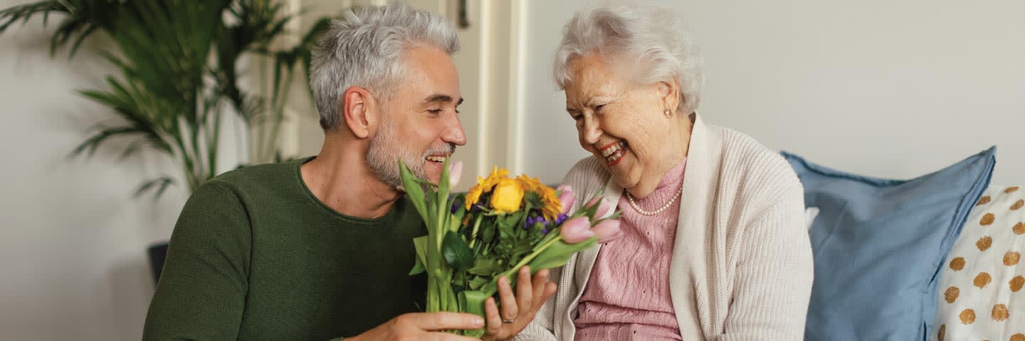 Elderly woman recieving flowers from a younger man