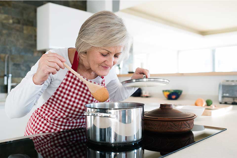 Elderly woman cooking pasta sauce on her stovetop.