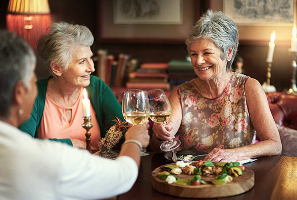 A group of senior women toasting with wine glasses inside a restaurant
